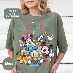 A woman wearing a green t-shirt with a colorful graphic of Disney characters from the theme park.
