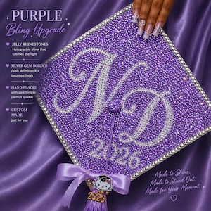 Pode incluir: Um chapéu de formatura roxo coberto com strass de gelatina e uma borda de gema prateada. O chapéu apresenta as iniciais "ND" em strass prateados e o ano de "2026". Inclui um borla e um pingente Hello Kitty. O texto "Purple Bling Upgrade" é visível.