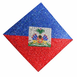 May include: A diamond-shaped graduation cap, split horizontally into red and blue sections, with a central square featuring the Haitian coat of arms. The cap is covered in sparkling embellishments.