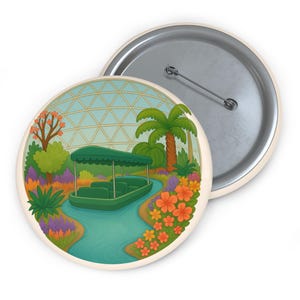 May include: A round button pin featuring a green boat on a blue river surrounded by colorful flowers and palm trees. The background shows a geodesic dome. The pin has a metal back and a pin clasp.