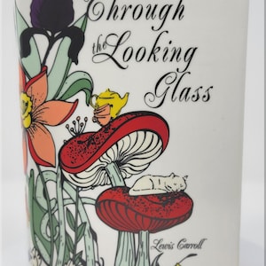 May include: White ceramic vase with a colorful illustration from "Through the Looking Glass" by Lewis Carroll. The design includes a purple iris, orange flowers, red mushrooms, a sleeping cat, and a yellow teapot. The text "Through the Looking Glass" is written in elegant script.
