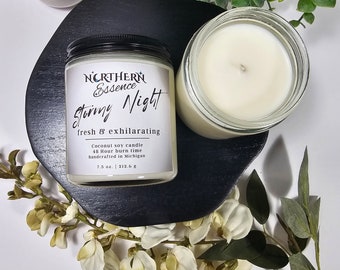 May include: A white coconut soy candle in a clear glass jar with a black lid. The label reads "NORTHERN Essence Stormy Night fresh & exhilarating Coconut soy candle 48 Hour burn time handcrafted in Michigan 7.5 oz. | 212.6 g"