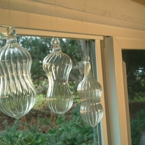 Könnte beinhalten: Drei klare Glaskugeln, die an einem Fenster hängen. Die Kugeln sind nussförmig und haben eine gerippte Textur.