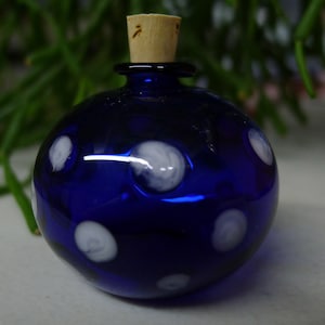 Puede incluir: Una botella redonda de vidrio azul cobalto con lunares blancos. La botella tiene un tapón de corcho. Es un objeto decorativo.