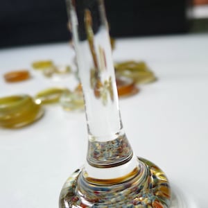 May include: A clear glass bottle stopper with a colorful, speckled base. The base is made of glass and has a variety of colors, including red, blue, green, and yellow.