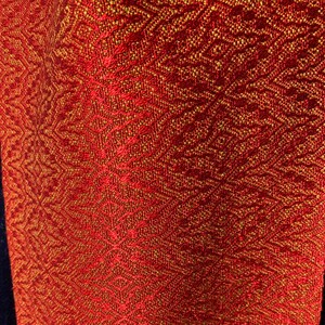 May include: Red fabric with a gold woven pattern. The fabric has a subtle sheen and a textured surface.