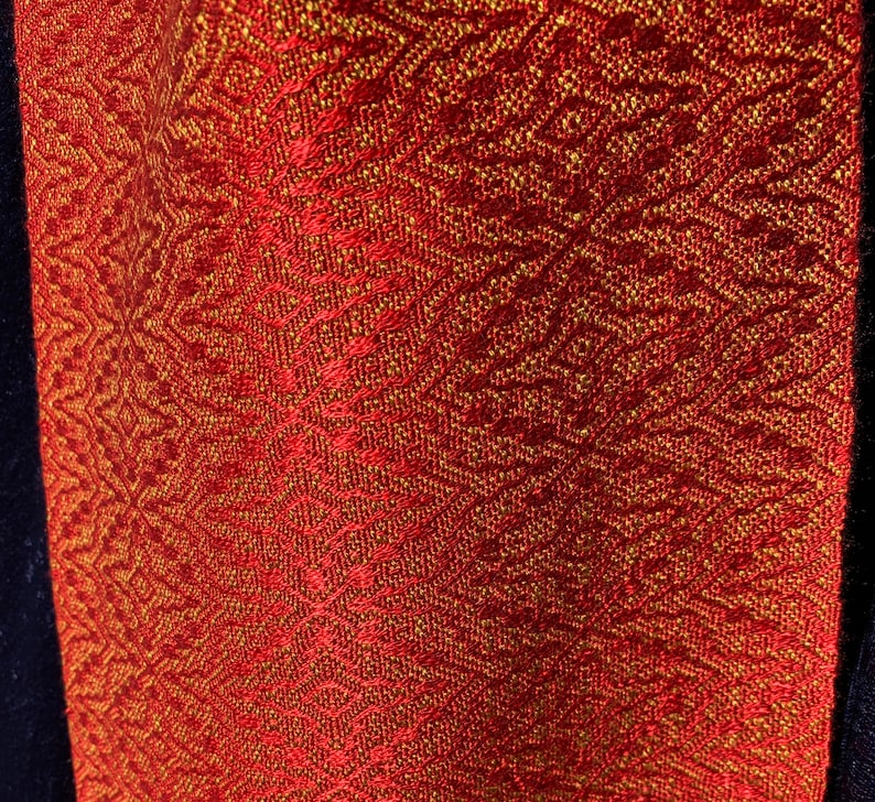 May include: Red fabric with a gold woven pattern. The fabric has a subtle sheen and a textured surface.
