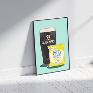 May include: A framed print featuring a pint of Guinness and a packet of Scampi Fries. The Guinness glass is black with the white harp logo. The Scampi Fries packet is yellow with blue text, including "Scampi Fries" and "Scampi & Lemon".