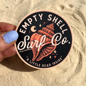 May include: Round sticker with a black background and a peach-colored seashell illustration. The sticker reads "EMPTY SHELL Surf Co." in white script, with the phrase "A LITTLE DEAD INSIDE" at the bottom. A crescent moon and stars are also featured.