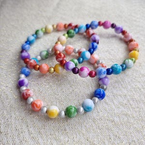 May include: Three colourful beaded bracelets. Each bracelet features a variety of round beads in shades of red, orange, yellow, green, blue, and purple. The beads are strung together with silver-coloured spacers and gold-coloured beads.