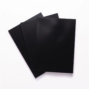 May include: A stack of three rectangular black sheets arranged in a fan-like formation. Each sheet is solid black with a smooth, matte finish and sharp, clean edges, overlapping slightly to reveal the layers beneath the top sheet.