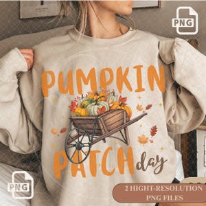 Puede incluir: Una sudadera beige de cuello redondo con un gráfico de una carretilla de madera llena de calabazas y hojas de otoño. El texto PUMPKIN PATCH day está impreso en letras grandes de color naranja y marrón sobre y bajo la ilustración.