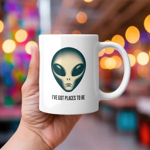 May include: White ceramic mug with a green alien face and the text "I've got places to be".