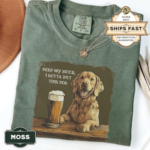 May include: Green t-shirt with a brown dog and a glass of beer. The text on the shirt reads "Hold my beer, I gotta pet this dog."