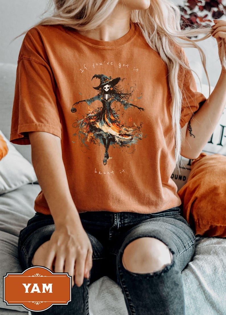 A spooky yet chic t-shirt design featuring a dancing skeleton girl in a flowing gown, holding a jack-o-lantern, with the phrase If You've Got It, Haunt It. Perfect for Halloween enthusiasts, gothic fashion fans, and stylish Halloween events.