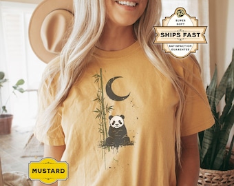 Op de afbeelding: Een mosterdgeel T-shirt met een zwart-witte pandabeer afbeelding. De panda zit voor een bamboestok en een halve maan. Het shirt heeft een verweerde look en de tekst "MUSTARD" is zichtbaar in de linkerbenedenhoek.