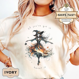 A spooky yet chic t-shirt design featuring a dancing skeleton girl in a flowing gown, holding a jack-o-lantern, with the phrase If You've Got It, Haunt It. Perfect for Halloween enthusiasts, gothic fashion fans, and stylish Halloween events.