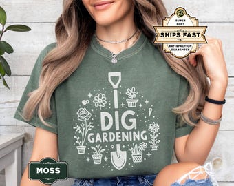 May include: Moss green t-shirt featuring the words "DIG GARDENING" in white, with flower and shovel illustrations. The shirt has a crew neck and short sleeves. The image also includes a "SHIPS FAST" graphic.