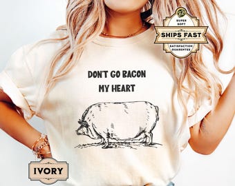May include: A white t-shirt with the text "Don't go bacon my heart" and a black and white illustration of a pig. The shirt is available in ivory.