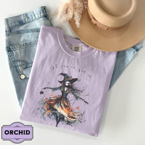 A spooky yet chic t-shirt design featuring a dancing skeleton girl in a flowing gown, holding a jack-o-lantern, with the phrase If You've Got It, Haunt It. Perfect for Halloween enthusiasts, gothic fashion fans, and stylish Halloween events.