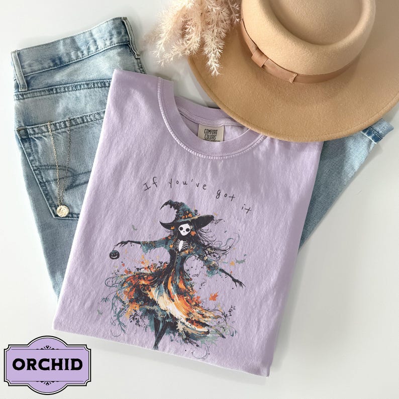A spooky yet chic t-shirt design featuring a dancing skeleton girl in a flowing gown, holding a jack-o-lantern, with the phrase If You've Got It, Haunt It. Perfect for Halloween enthusiasts, gothic fashion fans, and stylish Halloween events.