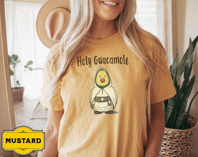 A humorous t-shirt design featuring an avocado dressed as a monk with a cross belt, perfect for food humor enthusiasts. Ideal for those who love avocado puns, funny Christian gifts, and funny phrase slogans for a unique twist on Holy Guacamole.