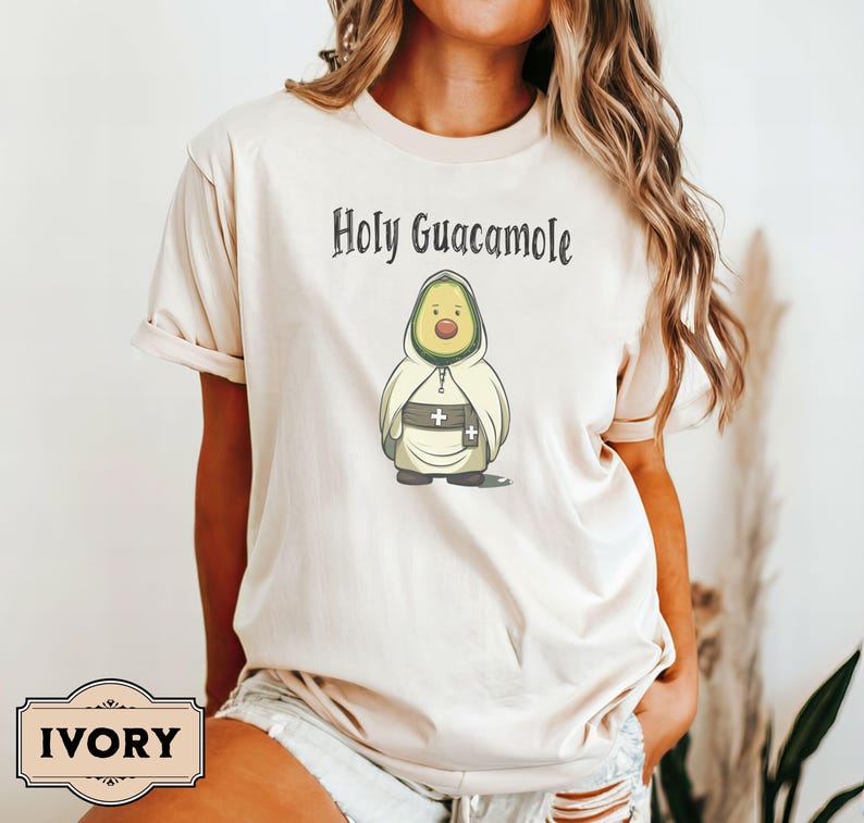 A humorous t-shirt design featuring an avocado dressed as a monk with a cross belt, perfect for food humor enthusiasts. Ideal for those who love avocado puns, funny Christian gifts, and funny phrase slogans for a unique twist on Holy Guacamole.