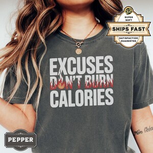 May include: A dark gray t-shirt with the text "EXCUSES DON'T BURN CALORIES" in white lettering. The text is surrounded by a red flame design.