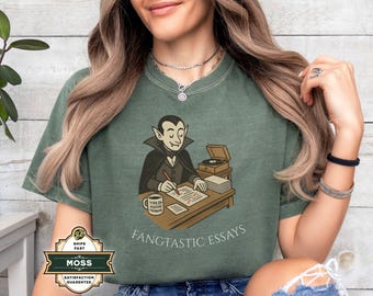 May include: Green t-shirt with a cartoon vampire writing at a desk. The vampire is wearing a black cape and tuxedo. The text "FANGTASTIC ESSAYS" is printed below the image. A coffee mug reads "TYPE OF POSITIVE FEEDBACK".