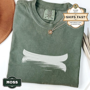 May include: A green t-shirt featuring a white canoe graphic and the text "MOSS" printed in the bottom left corner. The shirt is made from a soft, comfortable fabric and has a relaxed fit.