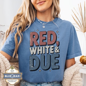 May include: A blue t-shirt featuring the text "RED, WHITE & DUE" in red, white, and blue. The design has a vintage, worn appearance. The text is in a bold, blocky font with a shadow effect. The shirt is a short-sleeved, crew neck style.