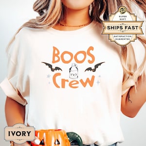 May include: A white t-shirt with the text "Boo's Crew" in orange letters. A black bat silhouette is above the word "Boo's" and a cartoon bottle with the text "XXX" is between the words "Boo's" and "Crew".