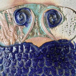 Può includere: Una scultura di gufo in ceramica dipinta in blu e bianco. Il gufo ha grandi occhi rotondi e un corpo testurizzato. Il gufo è in piedi su due piedi con tre dita ciascuno.