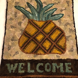 May include: A welcome mat with a brown background and a green pineapple with a yellow body and brown stripes. The word "WELCOME" is written in green letters on the bottom of the mat.