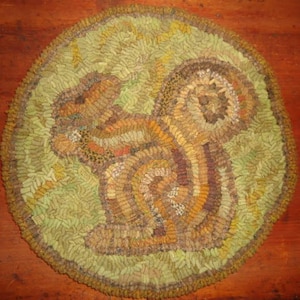 May include: A round, green, brown, and yellow rug with a squirrel design. The rug is made of fabric scraps and is a traditional folk art piece.