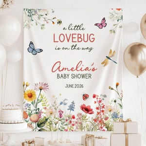 May include: A baby shower banner with the text "a little LOVEBUG is on the way" and "Amelia's BABY SHOWER JUNE 2026". The banner features floral and insect illustrations, including butterflies and a dragonfly. White balloons and gifts are also present.