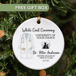 May include: A white ceramic ornament with a gold string for hanging. The ornament features text and illustrations related to a veterinary white coat ceremony. The text includes "White Coat Ceremony", "University of Your Choice", and a name and date.