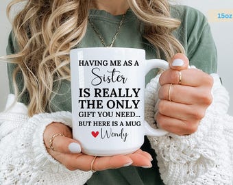 May include: White ceramic mug with black text that reads "Having me as a Sister is really the only gift you need... But here is a mug Wendy". The mug has a red heart next to the name Wendy. The mug is 15 ounces.