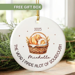 May include: White ceramic ornament with a watercolor illustration of bread in a basket. The text reads "2025 The Year I Made a Lot of Sourdough" and "Michelle". Includes a gold hanging string.