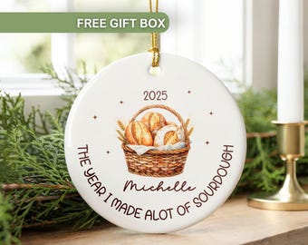 May include: White ceramic ornament with a watercolor illustration of bread in a basket. The text reads "2025 The Year I Made a Lot of Sourdough" and "Michelle". Includes a gold hanging string.