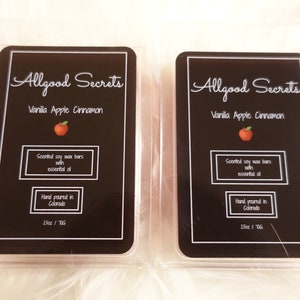 May include: Two rectangular wax melt bars in clear plastic packaging. Each bar has a black label with white text that reads "Allgood Secrets Vanilla Apple Cinnamon." The label also states "Scented soy wax bars with essential oil" and "Hand poured in Colorado."