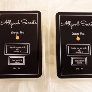 May include: Two rectangular wax melts with black labels. The labels read "Allgood Secrets Orange Peel" with an orange graphic. Text includes "Scented soy wax candle with essential oil" and "Hand poured in Colorado". Each melt is 2.5oz / 71g.