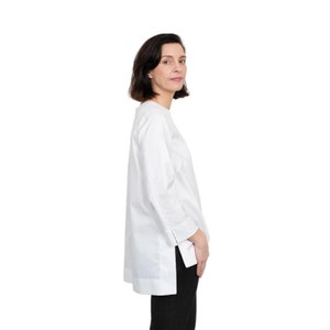 May include: A white long-sleeved shirt with a side slit detail. The shirt has a relaxed fit and a slightly rounded neckline.