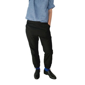 May include: A person wearing black pants with a cuffed hem, a light blue shirt, and black shoes with blue socks.