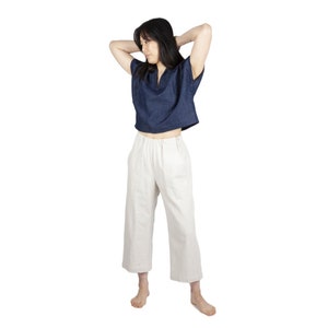 May include: A woman wearing a dark blue cropped top with a v-neck and short sleeves, paired with white wide-leg pants.