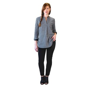 May include: A woman wearing a black and white gingham shirt with a v-neck and long sleeves. She is also wearing black skinny jeans and black ankle boots.