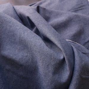 May include: Close-up of a blue denim fabric with a textured surface. The fabric is folded and wrinkled, showing the natural texture of the material.