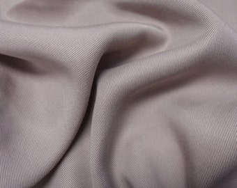 May include: A close-up of a soft, smooth, light gray fabric with a subtle ribbed texture. The fabric is draped and folded, creating a sense of movement and texture.