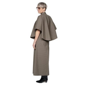 May include: A brown and white plaid cape with short sleeves and a wide collar. The cape is worn over a matching plaid skirt.