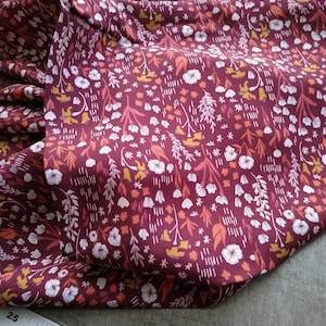 May include: A close-up of a burgundy fabric with a white, orange, and yellow floral pattern. The fabric is folded and a ruler is visible in the bottom right corner.